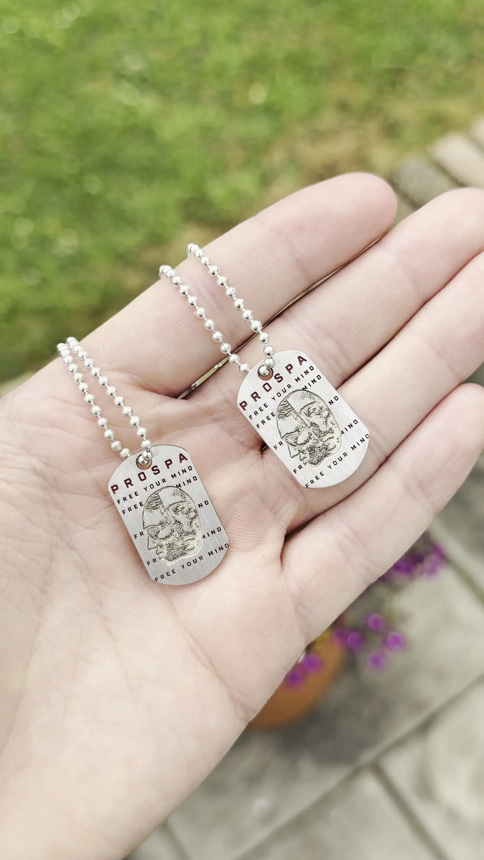 Two engraved dog tags on ball chains held in a palm