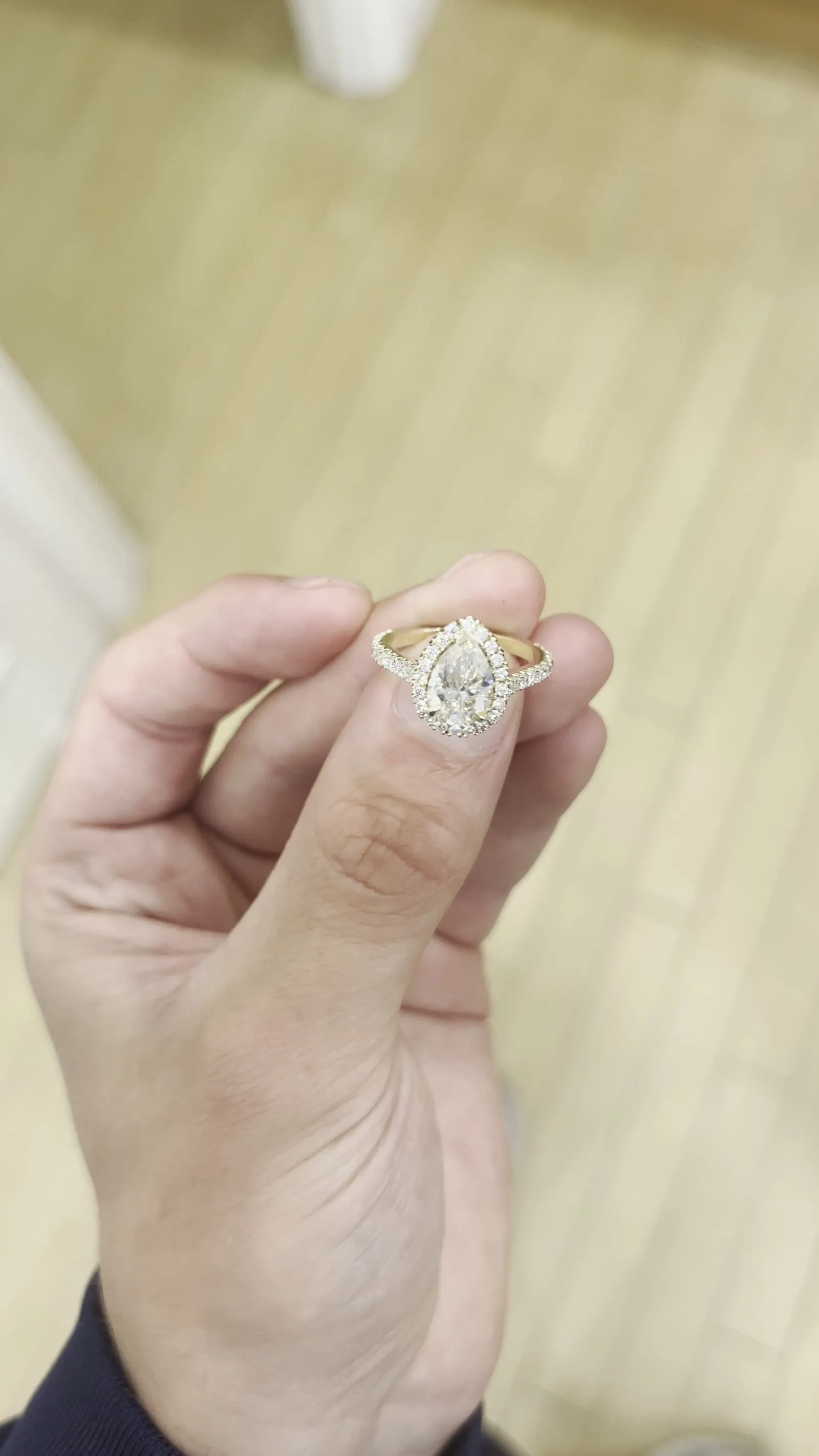 A pear-cut engagement ring in yellow gold held between finger and thumb